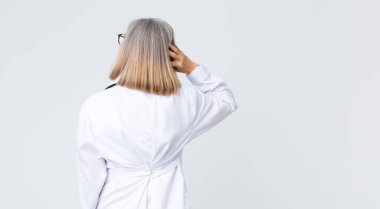 Orta yaşlı doktor kadın düşünüyor ya da şüphe ediyor, kafasını kaşıyor, şaşkın ve şaşkın hissediyor, arkaya ya da arkaya bakıyor.