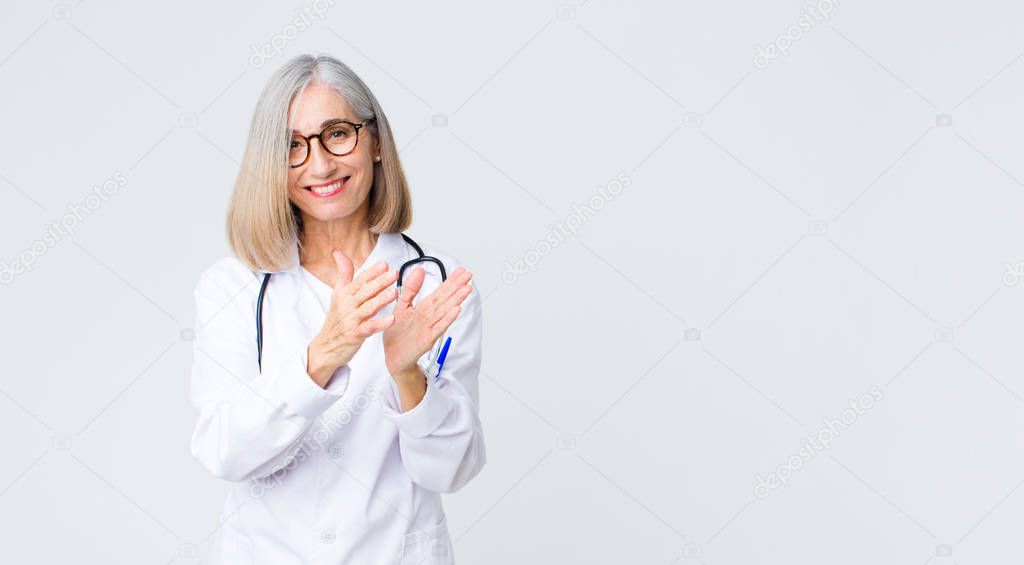 middle age doctor woman feeling happy and successful, smiling and clapping hands, saying congratulations with an applause