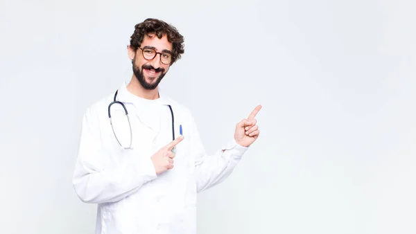 Młody Lekarz Uśmiecha Się Szczęśliwie Wskazując Bok Górę Obiema Rękami — Zdjęcie stockowe