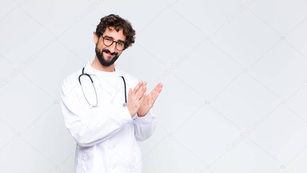 young doctor man feeling happy and successful, smiling and clapping hands, saying congratulations with an applause against copy space wall