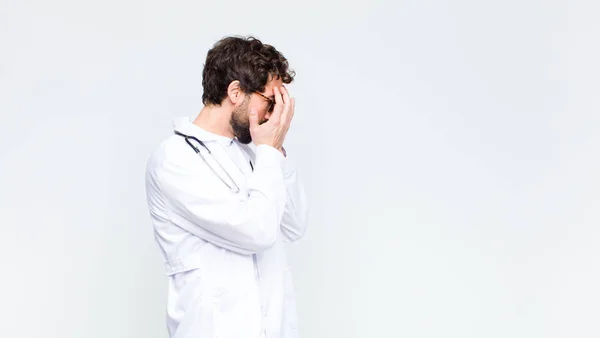 若い医者の男が手で目を覆い絶望の悲しい 欲求不満そうな表情で 泣いて コピースペースの壁に対するサイドビュー — ストック写真
