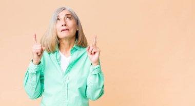 Orta yaşlı havalı kadın şaşırmış, şaşırmış ve ağzı açık görünüyor, iki eliyle uzayı işaret ediyor.