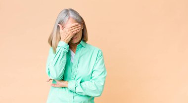 Orta yaşlı, havalı bir kadın stresli, utanmış ya da üzgün görünüyor, baş ağrısı var, yüzünü elle kapatıyor.