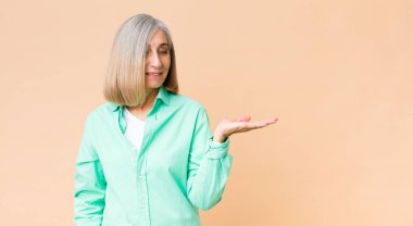 Orta yaşlı, havalı bir kadın mutlu ve güler yüzlü bir şekilde elinde tuttuğu bir nesneye ya da konsepte bakıyor.