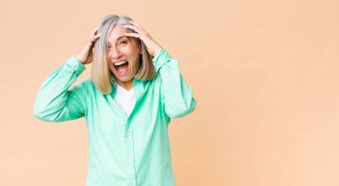 Orta yaşlı havalı bir kadın el ele tutuşuyor, ağzı açık, son derece şanslı, şaşırmış, heyecanlı ve mutlu.