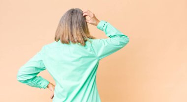 Orta yaşlı havalı bir kadın bilgisiz ve kafası karışık hissediyor, bir çözüm düşünüyor, eli kalçasında, diğeri kafasında, dikiz aynasından.