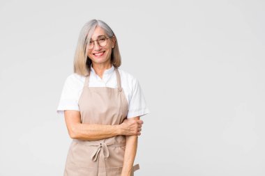 Orta yaşlı fırıncı kadın utangaç ve neşeli bir şekilde gülüyor. Düz duvara karşı dostane, olumlu ama güvensiz bir tutum sergiliyor.