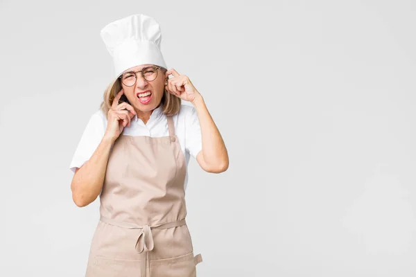 Kobieta Piekarz Średnim Wieku Wygląda Wściekłą Zestresowaną Rozdrażnioną Zakrywając Uszy — Zdjęcie stockowe