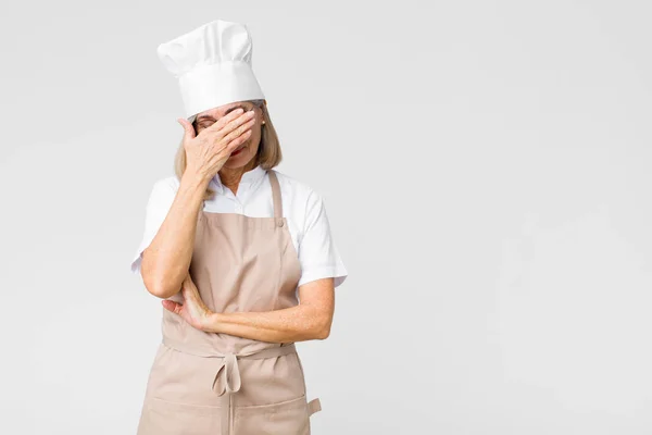 中年のパン屋の女性は 顔を平らな壁に対して手で覆い 頭痛の種で ストレスや恥じらいや動揺を見て — ストック写真