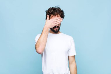 Genç çılgın sakallı adam tek eliyle gözlerini kapatıyor korkmuş ya da endişeli, merak ediyor ya da körü körüne düz duvara karşı bir sürpriz bekliyor.