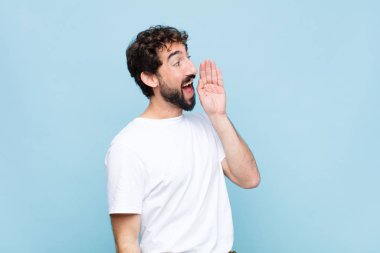 Genç çılgın sakallı adam profili, mutlu ve heyecanlı görünüyor, bağırıyor ve düz duvara karşı kopyalamak için çağırıyor