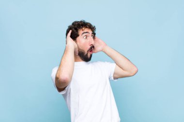 Genç, sakallı, ağzı açık genç bir adam korkunç bir hata yüzünden dehşete düşmüş ve şok olmuş görünüyor. Duvara karşı el kaldırıyor.