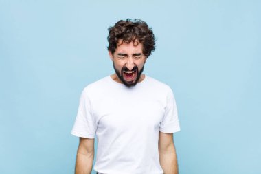 Genç çılgın sakallı adam agresif bir şekilde bağırıyor. Kızgın, sinirli ya da sinirli görünüyor. Düz duvara karşı hayır diye bağırıyor.