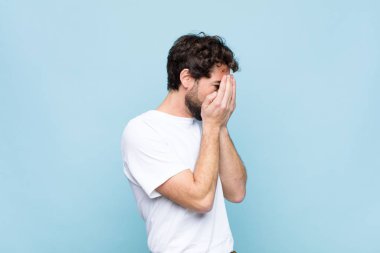 Genç, çılgın, sakallı, üzgün, hayal kırıklığına uğramış bakışlarıyla gözleri kaplayan, ağlayan, düz duvara bakan bir adam.