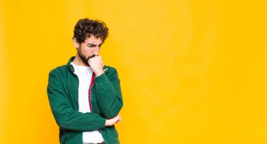 Genç çılgın sakallı adam ciddi, düşünceli ve endişeli, elleri çenesine yaslanmış bir şekilde duvara bakıyor.