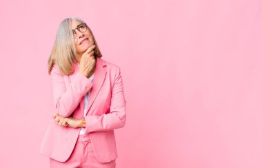 Orta yaşlı, düşünceli, kuşkulu ve kafası karışık, farklı seçenekleri olan, düz duvara karşı hangi kararı vereceğini merak eden havalı bir kadın.