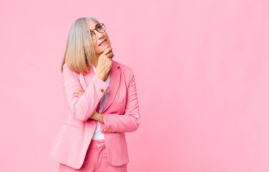 Orta yaşlı havalı bir kadın düşünceli, meraklı ya da hayal kuruyor, hayal kuruyor ve düz duvara karşı boşluğu kopyalamak istiyor.