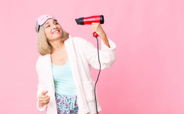 Orta yaşlı kadın saç kurutma makinesiyle gece elbisesi giyiyor.