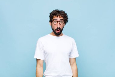 Mavi duvarda gözlüklü genç sakallı adam.