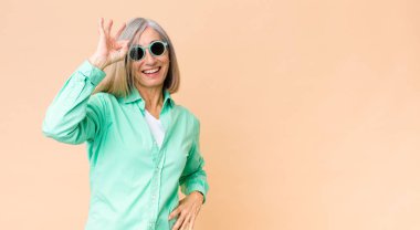 Orta yaşlı güzel kadın fotokopi duvarına güneş gözlüğü takıyor.