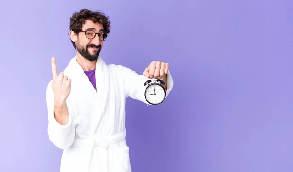 Young Crazy Bearded Man Wearing Bathrobe Holding Alarm Clock — Stock Photo, Image