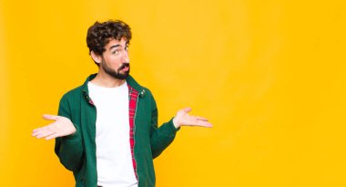Genç çılgın sakallı adam şaşkın ve şaşkın hissediyor, doğru cevap veya karardan emin değil, düz duvara karşı bir seçim yapmaya çalışıyor.