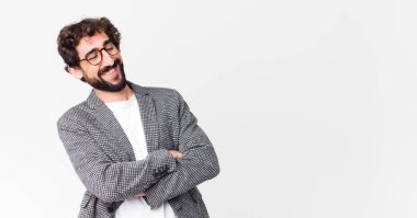 Genç çılgın iş adamı kollarını kavuşturup mutlu bir şekilde gülüyor, rahat, pozitif ve tatmin olmuş bir şekilde düz duvara dayanıyor.