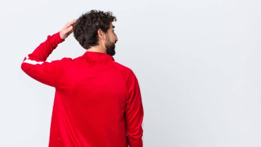 Genç sakallı adam, şaşkın ve kafası karışmış hissediyor. Kafasını kaşıyor ve fotokopi duvarına bakıyor.