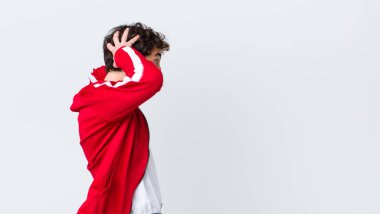 Genç sakallı adam geriden bakıyor. Stresli, endişeli ya da korkmuş hissediyor. Elleri başının üstünde.