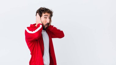 Delikanlı sakallı adam kötü bir şekilde şok olmuş, korkmuş ya da endişeli görünüyor ağzı sonuna kadar açık ve her iki kulağını da fotokopi duvarına karşı eliyle kapatıyor.