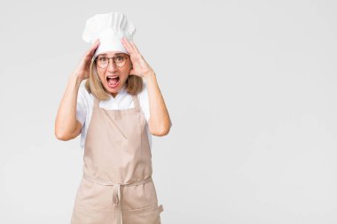 Orta yaşlı fırıncı kadın el ele tutuşuyor, ağzı açık, son derece şanslı, şaşırmış, heyecanlı ve mutlu.