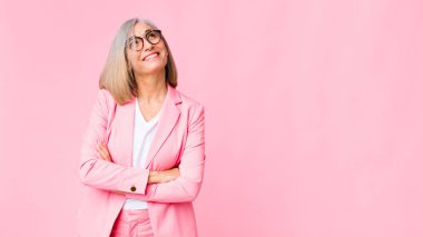 Orta yaşlı, havalı bir kadın mutlu, gururlu ve umutlu, merak eden ya da düşünen düz duvara yaslanmış çapraz kollarla fotokopi çekmek isteyen.