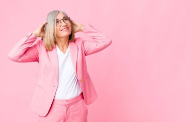 Orta yaşlı havalı bir kadın gülümsüyor ve rahatlıyor, tatmin oluyor ve kaygısız, pozitif gülüyor ve düz duvara yaslanıyor.