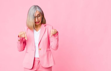 Orta yaşlı, ağzı açık, iki eliyle aşağıya bakan havalı bir kadın. Şaşırmış, şaşırmış ve şaşırmış görünüyor.