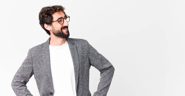 молодой сумасшедший бизнесмен выглядит счастливым, веселым и уверенным в себе, с гордостью улыбаясь и глядя в сторону с обеими руками на бедра к плоской стене
