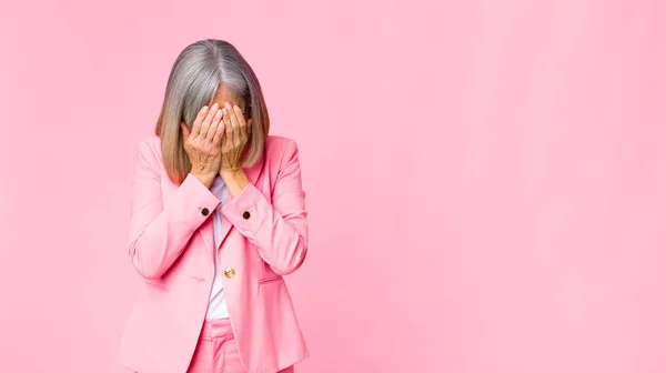 middle age cool woman feeling sad, frustrated, nervous and depressed, covering face with both hands, crying against flat wall