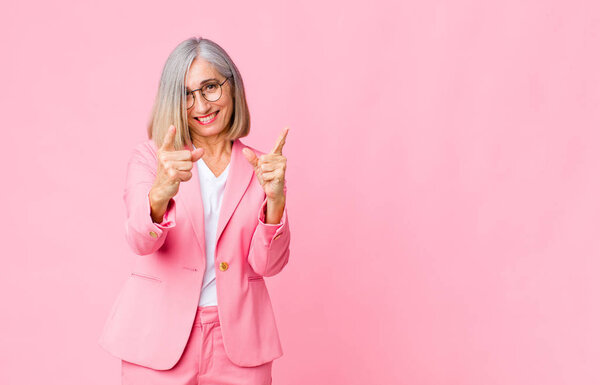 Среднего возраста прохладная женщина чувствует себя счастливой, прохладной, удовлетворенной, расслабленной и успешной, указывая на камеру, выбирая вас к плоской стене
