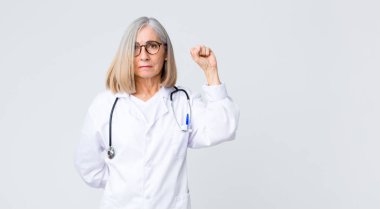 Orta yaşlı doktor kadın kendini ciddi, güçlü ve asi hissediyor, yumruğunu kaldırıyor, protesto ediyor ya da devrim için savaşıyor.