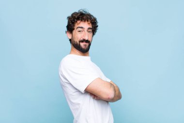 Genç çılgın sakallı adam kameraya çapraz kollarıyla gülümsüyor ve mutlu, kendinden emin, tatmin olmuş bir yüz ifadesi var.