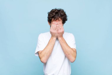 Genç çılgın sakallı adam üzgün, hayal kırıklığına uğramış, gergin ve depresif, yüzünü iki eliyle kapatmış, yassı duvara karşı ağlıyor.