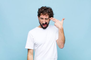 Genç, çılgın sakallı, mutsuz ve stresli görünen bir adam, intihar jesti, elle silah işareti yapıyor, kafasını düz duvara doğrultuyor.