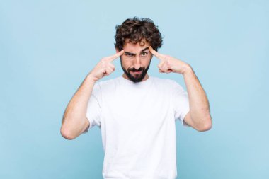 Ciddi ve konsantre görünümlü genç, çılgın sakallı adam düz duvara karşı zorlu bir sorun düşünüyor ve beyin fırtınası yapıyor.