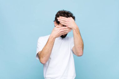 Genç çılgın sakallı adam kameraya hayır diyen iki eliyle yüzünü kapatıyor! Resimleri reddetmek ya da yasaklı fotoğrafları düz duvara yaslamak