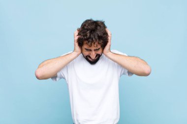 Genç çılgın sakallı adam kendini stresli ve hayal kırıklığına uğramış hissediyor. Yumruk yumruğa, yorgun, mutsuz ve migreni düz duvara dayanmış hissediyor.