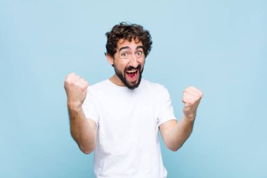 Genç çılgın sakallı adam mutlu, pozitif ve başarılı hissediyor, zaferi kutluyor, başarılar ya da düz duvara karşı iyi şanslar.