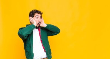 Genç, sakallı, ağzı açık genç bir adam korkunç bir hata yüzünden dehşete düşmüş ve şok olmuş görünüyor. Duvara karşı el kaldırıyor.