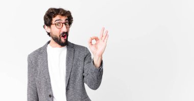 Genç çılgın iş adamı kendini başarılı ve tatmin olmuş hissediyor. Ağzı açık gülümsüyor. Düz duvara karşı el işareti yapıyor.