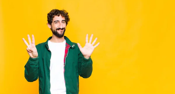 若い狂人髭の男は笑顔で友好的に見える前方に手で8番目または8番目を示し平らな壁に対してカウントダウン — ストック写真