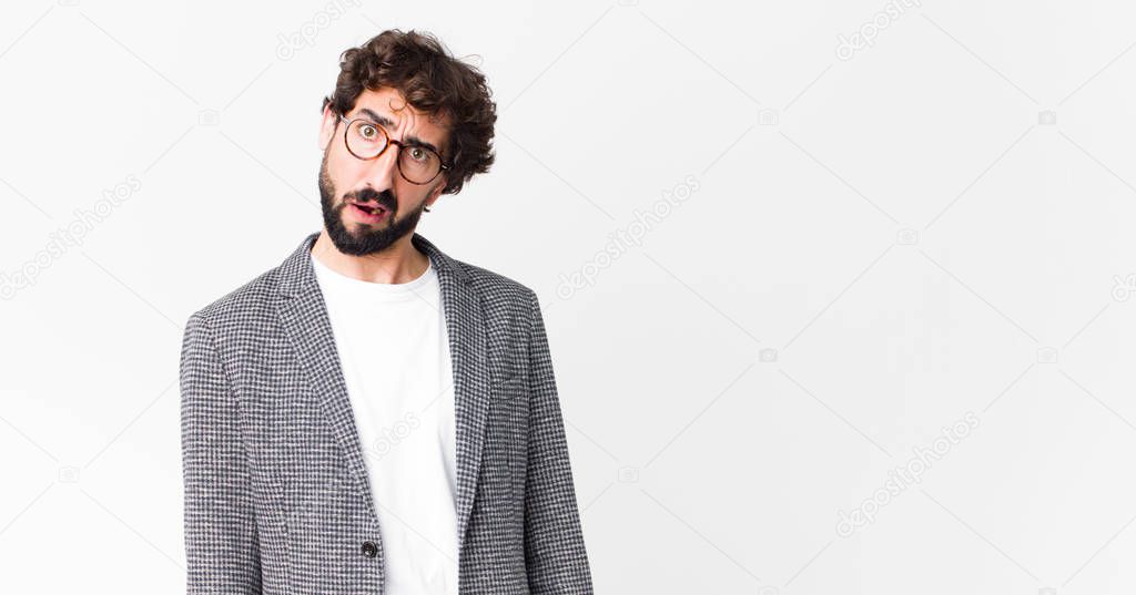 young crazy businessman feeling puzzled and confused, with a dumb, stunned expression looking at something unexpected against flat wall