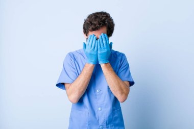 Genç adam üzgün, hayal kırıklığına uğramış, gergin ve depresif, iki eliyle yüzünü kaplayan, ağlayan. Coronavirus konsepti